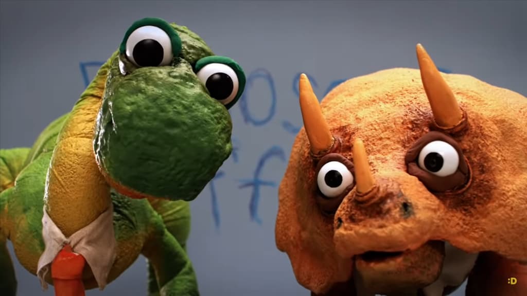 Two dinosaur puppets, one green and one orange, appear to converse against a blue backdrop